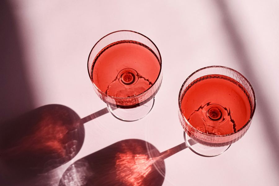 Two coupe glasses of a rosy pink drink casting shadows on a pink table