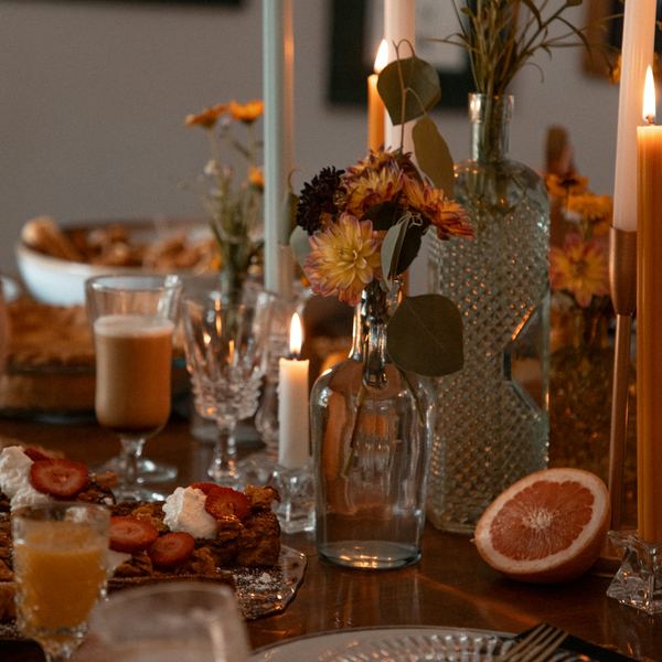 A candlelit party table with flowers in glass bottles, glassware and shared plates