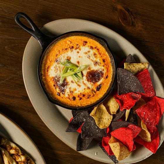 Skillet queso topped with green onions, with a pile of tortilla chips
