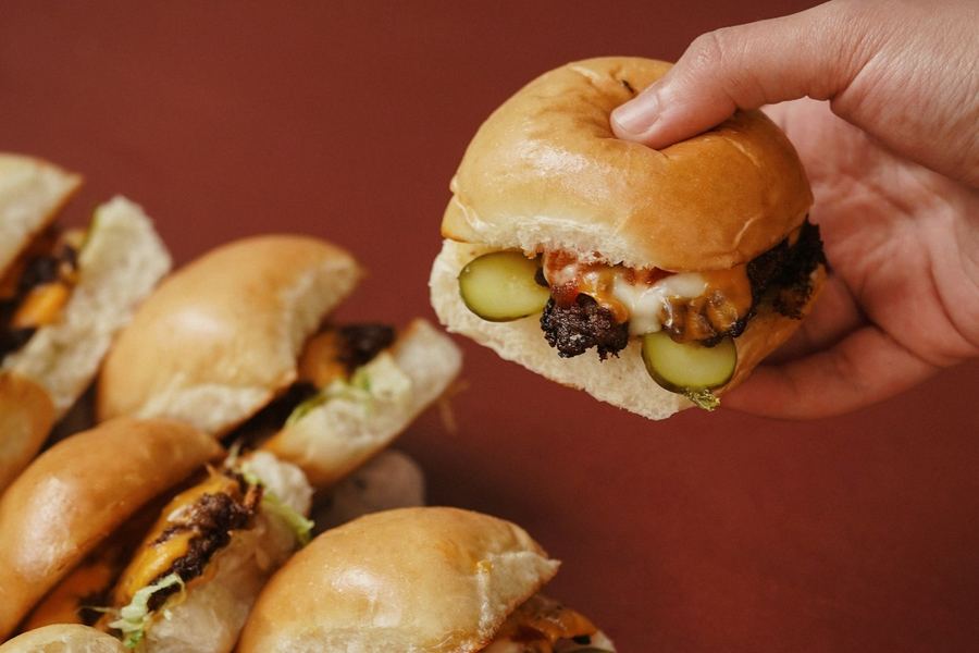 A hand reaching for a cheeseburger slider from a pile of sliders